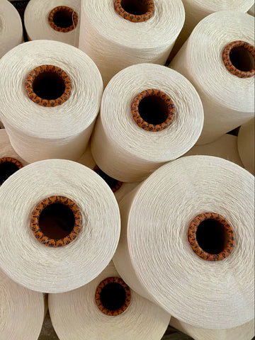 A close-up pile of large off-white or cream spools of thread or yarn with brown cardboard cores, stacked together.